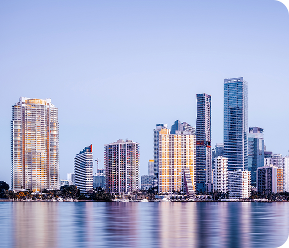 Skyline of a modern city with tall skyscrapers and apartment buildings, reflecting the innovative spirit of Secure & Insure MSPs in CyberSecurity, mirrored in calm water under a clear blue sky.